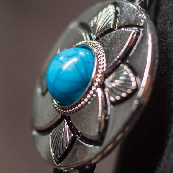 Close-up of an Outback Bolo Tie with a blue stone and silver design on a blurred background